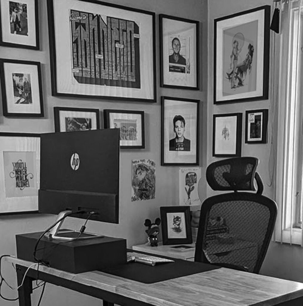 oh dang! office - desk with a computer monitor, and an open graphic design book and art prints on the wall adjacent to the desk